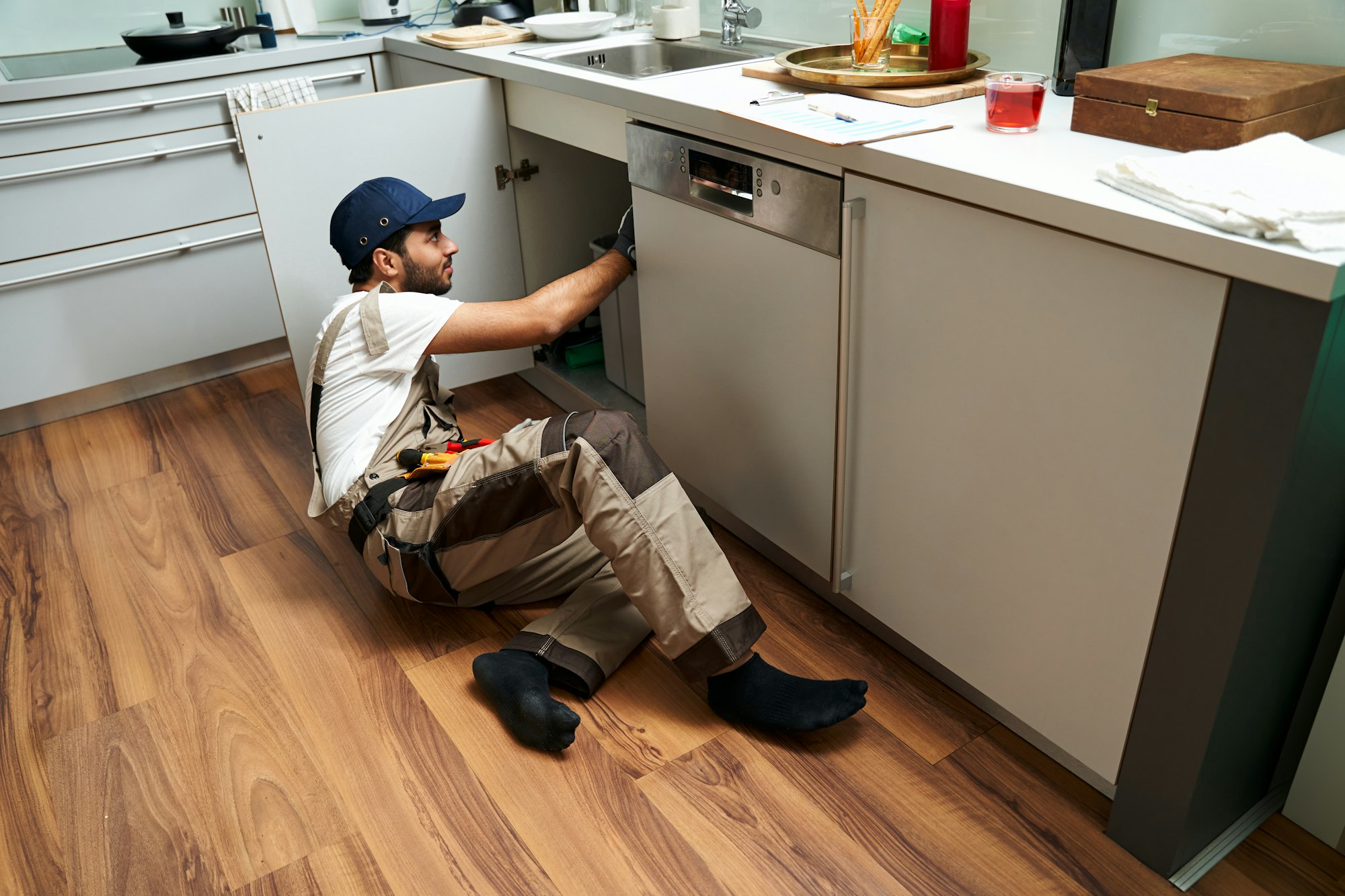 A professional male plumber in uniform is repairing a kitchen sink at home