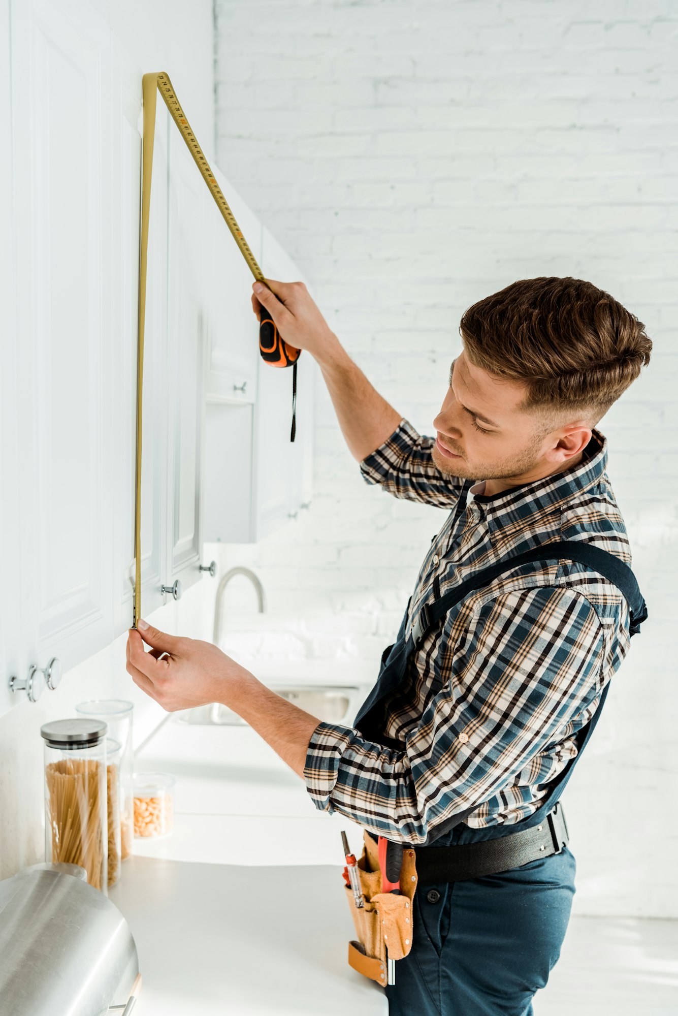 installer in overalls measuring white kitchen cabinet